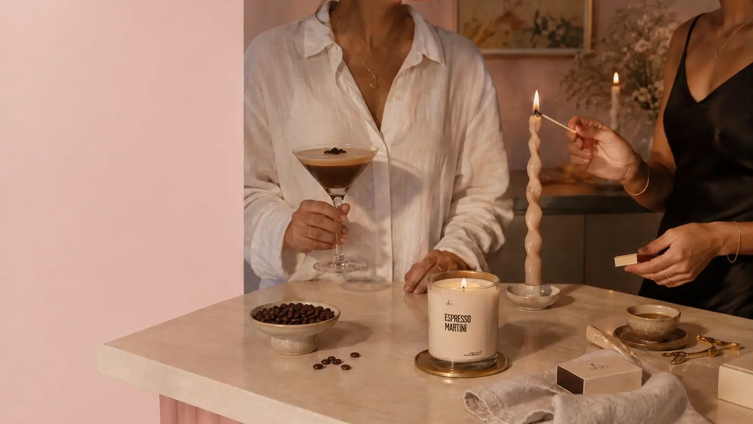 An Espresso Martini candle lit on a marble counter, beside a bowl of coffee beans.